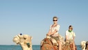Junge Menschen reiten auf Kamelen am Strand