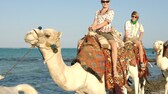 Junge Menschen reiten auf Kamelen am Strand