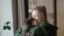 Graue Hsukatze sitzt auf dem Arm einer jungen Frau und beißt ihr zärtlich in die Nase, während sie lacht