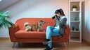 Frau hält eine Kamera in der Hand und sitzt Hund auf einem roten Sofa.