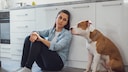 Eine traurige Frau sitzt neben ihrem Hund auf dem K&uuml;chenboden