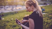 Frau sitzt im Park und hält ihr Smartphone in der Hand