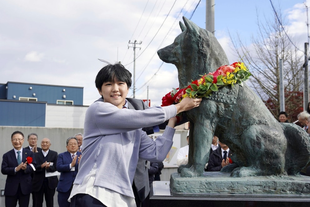 Junge legt der Statue von Hachiko in Japan eine Bluemgirlande um