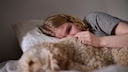 Eine weinende junge Frau liegt im Bett neben ihrem Hund