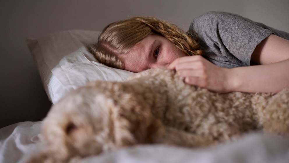 Eine weinende junge Frau liegt im Bett neben ihrem Hund