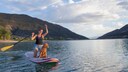 Eine Frau kniet auf ihrem Stand-Up Paddle mit ihrem Hund.