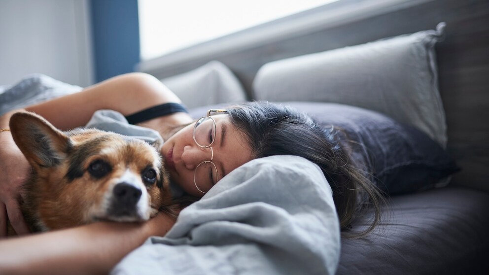 Frau kuschelt mit ihrem Hund im Bett