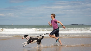 Junge Frau und Hund rennen gemeinsam am Strand