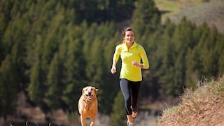 Eine Frau joggt mit ihrem Hund über eine Lichtung