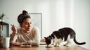 Frau sitzt mit Katze am Tisch und frühstückt zusammen mit dem Tier