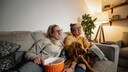 Gleichgeschlechtliches P&auml;rchen schaut mit Hund auf der Couch Fernsehen