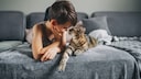 Kleiner Junge und Katze liegen zusammen auf der Couch