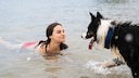 Frau im Wasser, Hund kommt schon nass auf sie zu.