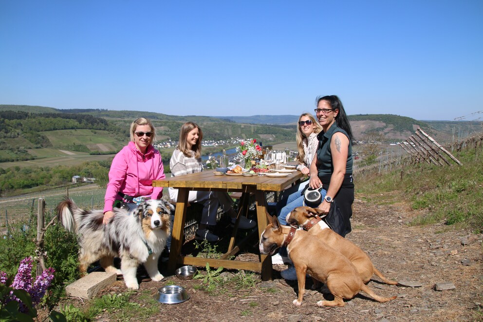 Four women sit with three dogs at a set table outdoors.