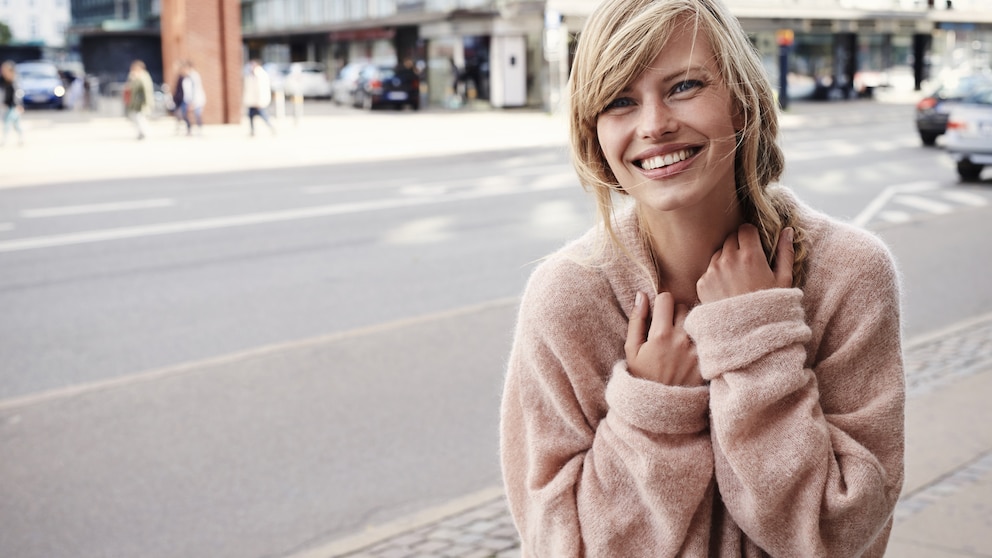 Lachende Frau auf Straße mit rosa Pullover