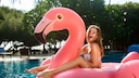 Junges Mädchen sitzt auf einem aufblasbaren Flamingo im Pool.