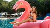 Junges Mädchen sitzt auf einem aufblasbaren Flamingo im Pool.