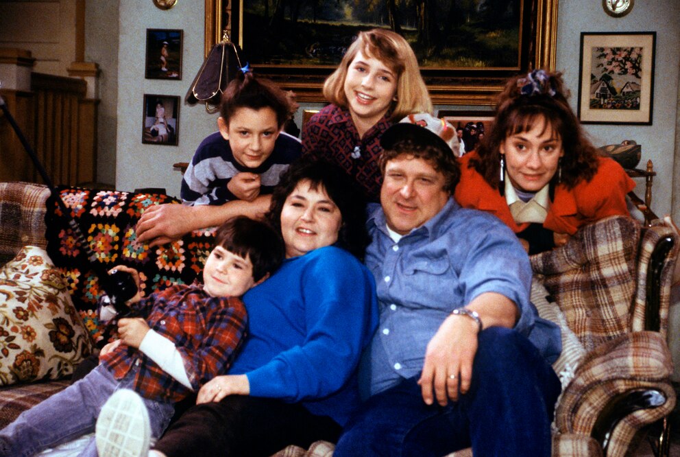  Der Original-Cast (v.l.n.r.: Michael Fishman, Roseanne Barr und John Goodman sitzen auf der legend&auml;ren Couch. Dahinter (v.l.n.r.): Sara Gilbert, Alicia Goransonund Laurie Metcalf