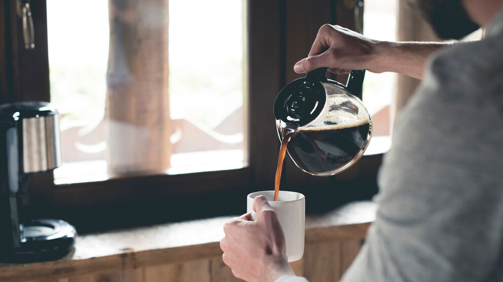 Mann gießt Kaffee in Tasse ein