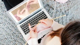 Frau strickt vor Laptop