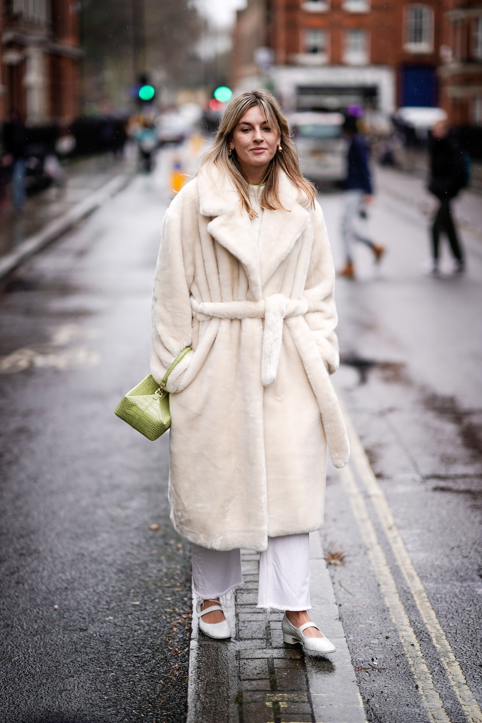 LONDON, ENGLAND - FEBRUARY 18: A guest wears earrings, a white fluffy coat, a lime green rectangular box bag, white pants, white ballerinas, during London Fashion Week February 2019 on February 18, 2019 in London, England. (Photo by Edward Berthelot/Getty Images)