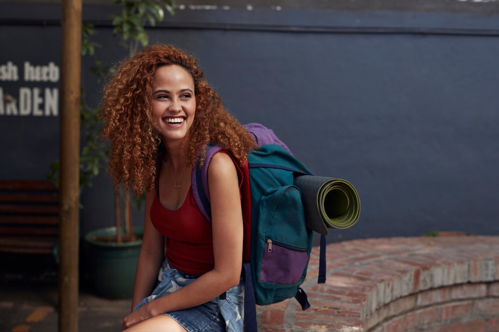 Young woman with backpack smiling, while sitting in courtyard