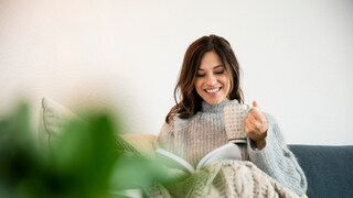 Hygge: Frau sitzt auf Sofa mit Decke und Tee