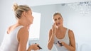 Frau cremt sich Gesicht mit Sonnencreme ein