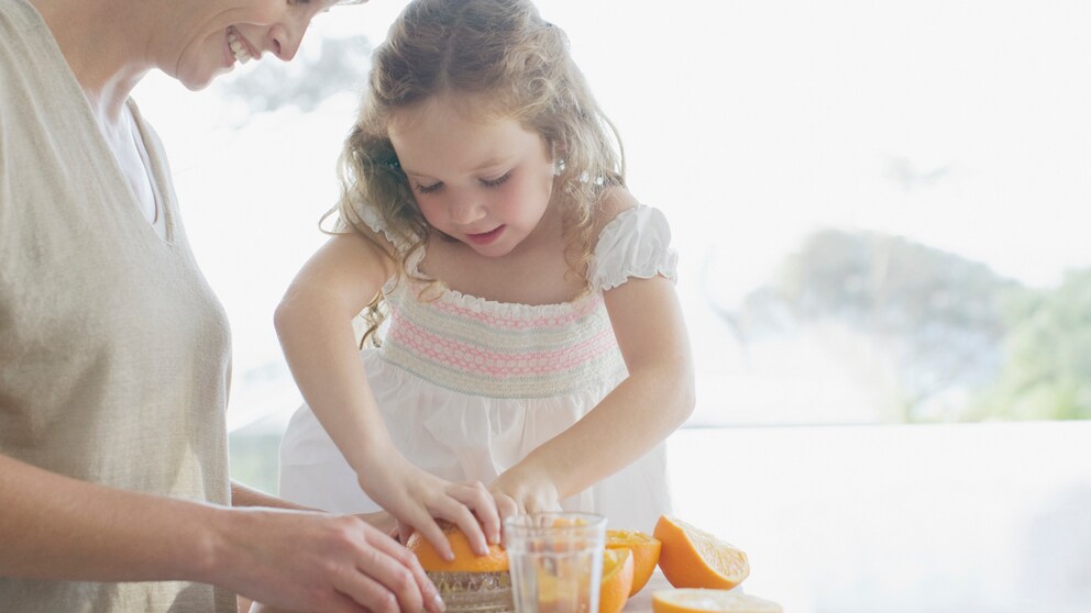 Frau und Kind pressen Saft aus Orangen