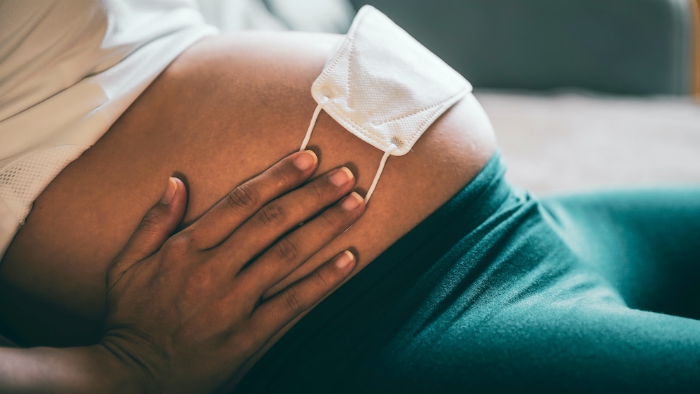 Schwangere Frau mit Mund-Nasen-Schutz auf dem Bauch