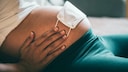 Schwangere Frau mit Mund-Nasen-Schutz auf dem Bauch