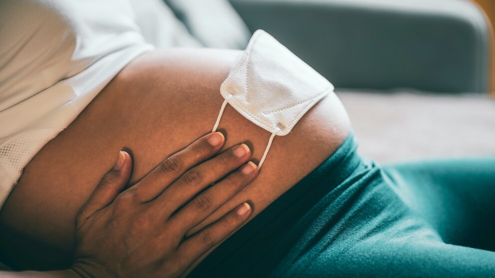 Schwangere Frau mit Mund-Nasen-Schutz auf dem Bauch