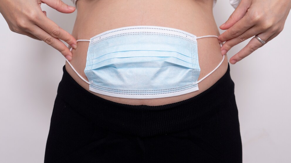 Schwangere Frau mit Maske vorm Bauch