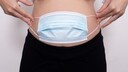 Schwangere Frau mit Maske vorm Bauch