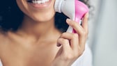 Lächelnde Frau benutzt elektrische Gesichtsbürste