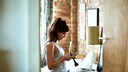 Frau mit Handy und Make-up Pinsel in Schlafzimmer