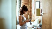 Frau mit Handy und Make-up Pinsel in Schlafzimmer