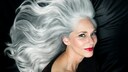 Frau mit langen, welligen, silbergrauen Haaren und klassischem Make-up, die seitlich in die Kamera lächelt