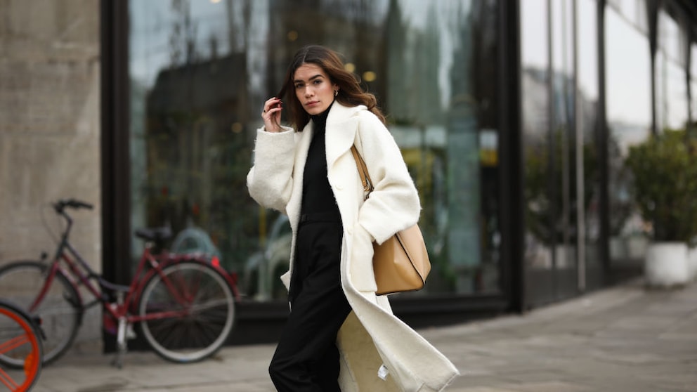 Junge Frau in cremefarbenem Mantel und schwarzem Outfit