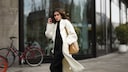 Junge Frau in cremefarbenem Mantel und schwarzem Outfit