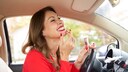 Reife Frau im Auto, die lachend Lippenstift korrigiert
