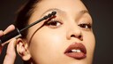 Close-up einer Lady, die Mascara „aufträgt“ mit braunem, glänzendem Lippenstift. Das Foto stammt sicher aus den 90ern, aber passt ja zur Ästhetik von heute