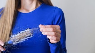 Frau in blauem Pulli mit Rundbürste mit vielen ausgefallenen Haaren.