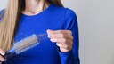 Frau in blauem Pulli mit Rundbürste mit vielen ausgefallenen Haaren.