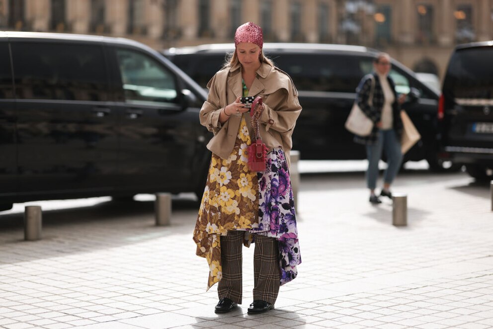 Dame bei der Pariser Fashion Week mit Cropped Trench in Beige und passender Stoffhose. Dazu kombiniert sie fancy Blumenkleidchen und ein Glitzer-Bandana. Nicht unbedingt ein Look für jeden Tag, aber mutig und ein Hingucker auf alle Fälle!