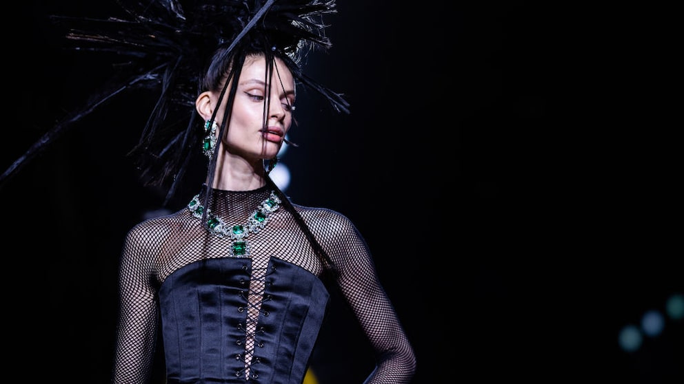 Model in schwarzem Mesh und Seidenkorsett mit spitzer Frisur und Smaragd-Schmuck. Da das die Show für den Herbst/Winter 23/24 ist – an den wir noch gar nicht denken wollen, aber – vielleicht bleibt uns der Smaragd-Trend erhalten