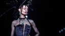 Model in schwarzem Mesh und Seidenkorsett mit spitzer Frisur und Smaragd-Schmuck. Da das die Show für den Herbst/Winter 23/24 ist – an den wir noch gar nicht denken wollen, aber – vielleicht bleibt uns der Smaragd-Trend erhalten