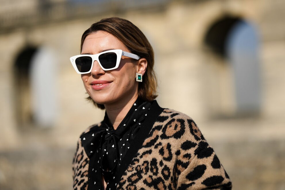 Dame mit Smaragdohrringen, Leo-Cardigan und schwarzer Bluse mit weißen Herzchen und weißer eckiger Sonnenbrille im Close-up. Ein Outfit, das ich nie kombinieren würde und mich aktuell frage, wieso nicht?! Bei ihr sieht das klasse aus!