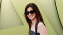 Anne Hathaway mit großer schwarzer Sonnenbrille, schwarzem Trägerkleid und großem Lächeln
