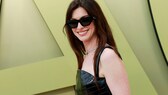 Anne Hathaway mit großer schwarzer Sonnenbrille, schwarzem Trägerkleid und großem Lächeln